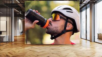 young cyclist with helmet and cycling goggles drinking water from his bottle, concept of freedom and sport in nature Wall mural