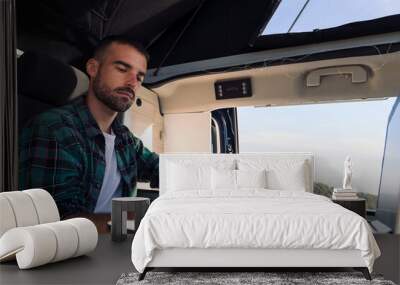 young man using his mobile phone and laptop from his camper van in the middle of nature, concept of freedom and digital nomad lifestyle Wall mural