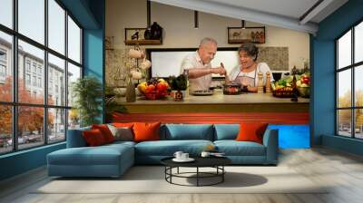 Happy Indian Asian gen x old aged senior lover couple pair modern home kitchen enjoy fun joy spend time indoor house female wife male man chef stir mix vegan food use spatula health care good habit Wall mural