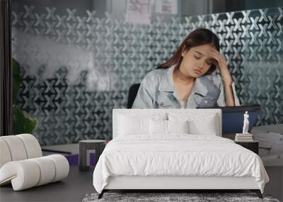 Indian busy young adult stress sad upset woman lady sitting chair hold pen use tablet do work day task writing book indoor job office teen girl staff feel bad tired suffer head ache pain health issue Wall mural