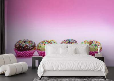 Mini cakes with icing and colorful sprinkles on pink background Wall mural