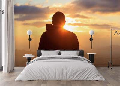 Silhouette of a man standing alone on the top of a mountain. Wall mural