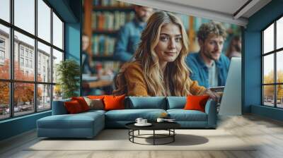 Young woman in a mustard sweater studying with a laptop in a library Wall mural