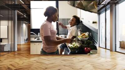 Black kid feeding mother with cooking food in the kitchen Wall mural