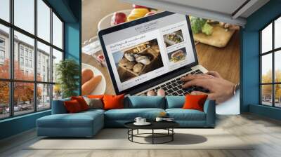 Caucasian man using a laptop in the kitchen searching for recipes Wall mural