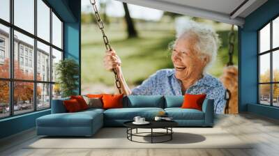 Cheerful senior woman on a swing at a playground Wall mural