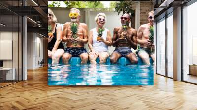 Group of diverse senior adults sitting at poolside holding pineapples together Wall mural