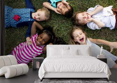 Group of kindergarten kids lying on the grass at park and relax with smiling Wall mural