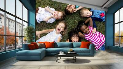 Group of kindergarten kids lying on the grass at park and relax with smiling Wall mural