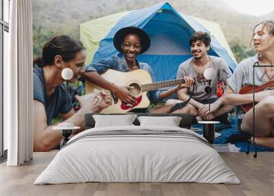 Group of young adult friends in camp site playing guitar and ukelele and singing together outdoors recreational leisure and friendship concept Wall mural