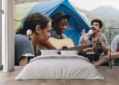 Group of young adult friends in camp site playing guitar and ukelele and singing together outdoors recreational leisure and friendship concept Wall mural