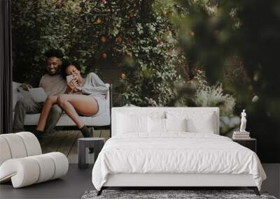 Happy black couple enjoying in the garden with a book and a smartphone Wall mural