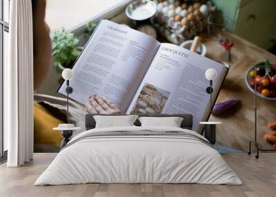 Happy woman reading a cookbook in the kitchen Wall mural