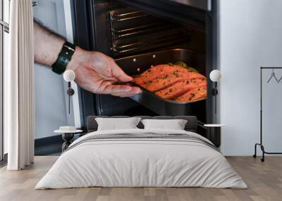 Man putting raw salmon steak into oven Wall mural