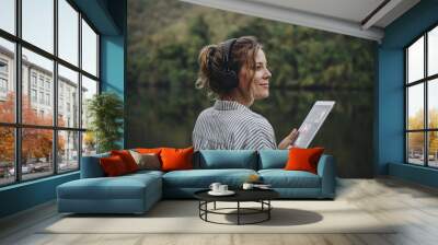 Woman alone in nature listening to music with headphones and digital tablet music and relaxation concept Wall mural