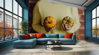 Woman in a yellow sweater holding pumpkins in her hands Wall mural