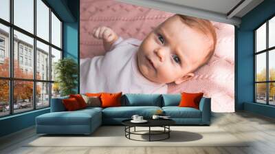 Cute two months old baby infant girl lying on pink blanket and looking at the camera with serious face Wall mural