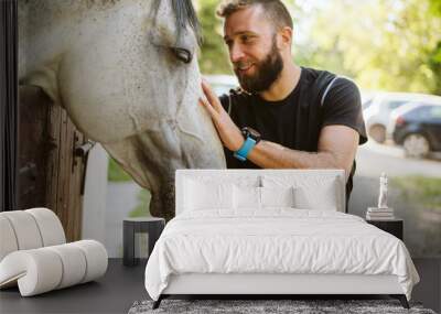 Summer day on the farm. Young man caress horse Wall mural