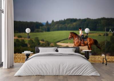 Horsewoman with horse galloping on a stubble field in summer photographed from the front from some distance.. Wall mural