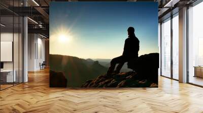 Hiker take relaxing on a rock and enjoying sunset at horizon. Vivid effect. Wall mural