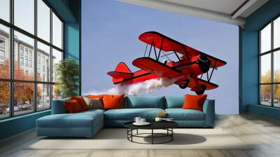 Red retro airplane (biplane) isolated on blue sky background. Vintage old red airplane & pilot flying in sky. View of red airplane & white smoke. Biplane condensation trail, smoky effect after plane Wall mural