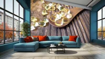 Vitamin D yellow pills on wood spoon on wooden background & soft sun light. Medicine gel tablets of vitamin d on table. Yellow vitamin D oil capsule keeps healthy while lack of sun - medicine concept Wall mural