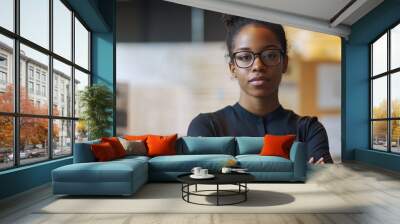 A young Black female architect stands confidently in a modern workspace, showcasing her professionalism and creativity. She embodies ambition and innovation. Wall mural