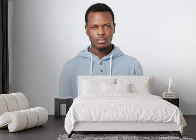 African man with serious expression looking at camera while posing against white studio wall. Wall mural