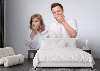 Mature woman and man giggling together covering their mouths with hands trying to be calm Wall mural