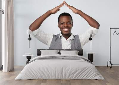 Portrait of a cheerful man holding hands over head like a roof house on gray background Wall mural