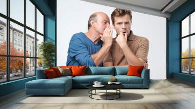 Senior man sharing secret or whispering gossips into his son ear. Telling family secret concept Wall mural