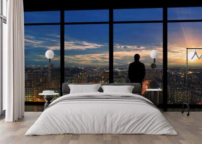 The male standing near the panoramic window against the bright sunset Wall mural