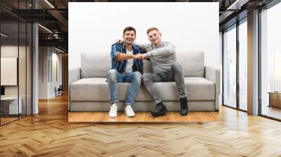 The two happy men on the sofa gesture on the white wall background Wall mural