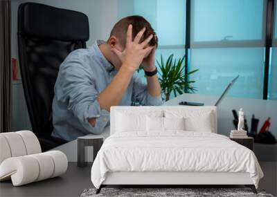 Tired or stressed young businessman sitting in front of computer in office. Wall mural