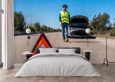 Young man preparing a red triangle to warn other road users of car breakdown Wall mural