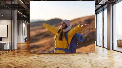 Portrait of young woman with arms outstretched to the sun in the mountain.	 Wall mural