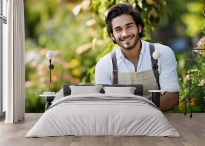 A cheerful young man in an apron posing in a vibrant flower garden, exuding happiness and a love for gardening. Wall mural