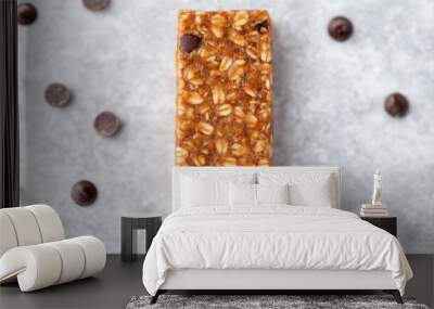 A granola bar made with peanut butter and chocolate chips rests on a gray surface, surrounded by scattered chocolate chips Wall mural