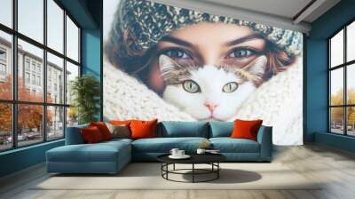 A woman and her cat, both wrapped in a cozy scarf, share an adorable close-up moment, emphasizing warmth and companionship. Wall mural