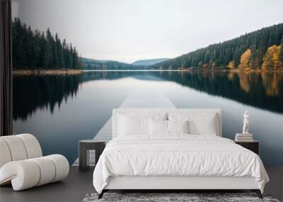 A wooden pier extends into a calm lake, reflecting the serene surroundings of trees and mountains at sunrise Wall mural