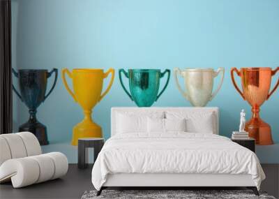 Colorful trophy awards of different styles and sizes are arranged on a plain blue background, representing various accomplishments Wall mural