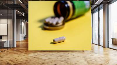 Medicine, pharmacy or dietary supplement concept. Bottle with pills and capsules over yellow backg
round. Side view. Wall mural