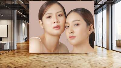 Close up portrait beauty shot of two young beautiful Asian girls looking at camera isolated on brown background. Wall mural