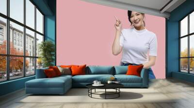 Happy young Asian woman feeling happiness and gesture pointing finger on isolated pink background with copy space. Wall mural