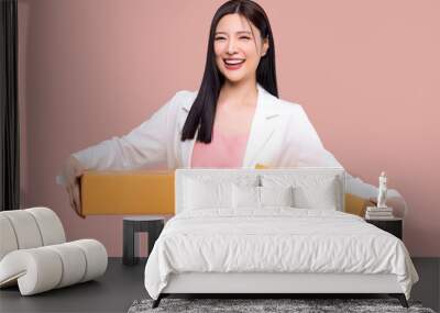 Portrait of young Asian business woman holding boxes, carry delivery goods, standing isolated over pink background. Wall mural