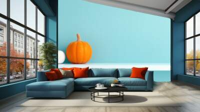 A white and an orange pumpkin sit on a white shelf against a light blue wall Wall mural