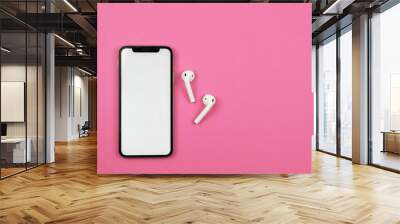 Mobile phone with wireless headphones on pink background. Wall mural