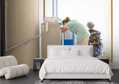 Aide soignante au travail accompagne personne agée en fauteuil roulant dans couloir hopital clinique maison de retraite Wall mural