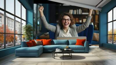 A young businesswoman in front of a laptop cheerfully celebrates success Wall mural