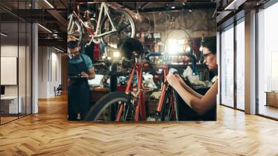 People, bicycle mechanic and fix with inspection for maintenance or small business at repair shop together. Young man, woman or cycling engineers working on bike with tools or equipment at workshop Wall mural